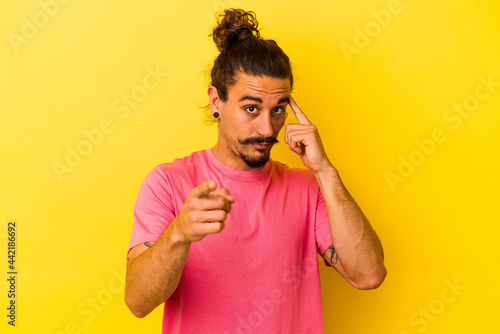 Young caucasian man with long hair isolated on yellow background pointing temple with finger, thinking, focused on a task.