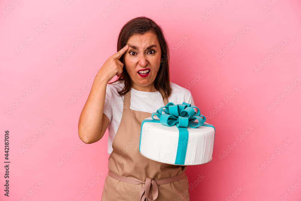Middle aged pastry chef woman holding a cake isolated on blue background showing a disappointment gesture with forefinger. Middle aged pastry chef woman holding a cake isolated on blue background showing a disappointment gesture with forefinger.