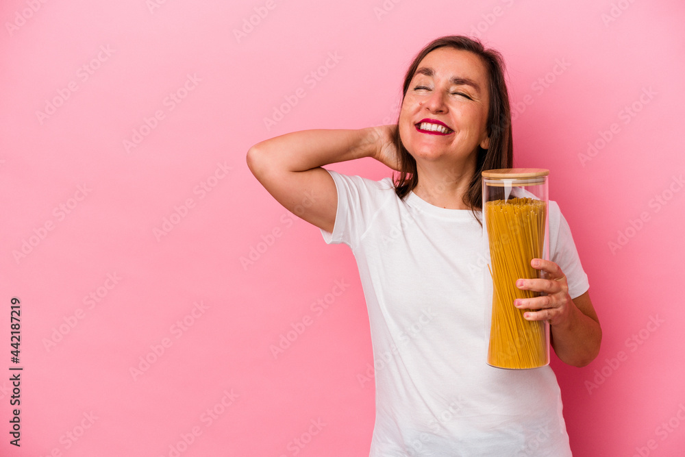 Middle age caucasian woman holding a pasta jar isolated on pink background touching back of head, thinking and making a choice. Middle age caucasian woman holding a pasta jar isolated on pink background touching back of head, thinking and making a choice.