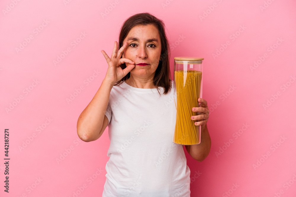 Middle age caucasian woman holding a pasta jar isolated on pink background with fingers on lips keeping a secret. Middle age caucasian woman holding a pasta jar isolated on pink background with fingers on lips keeping a secret.