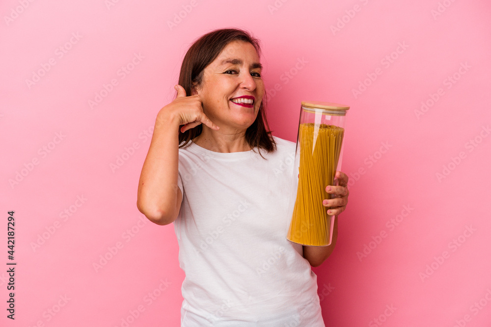 Middle age caucasian woman holding a pasta jar isolated on pink background showing a mobile phone call gesture with fingers. Middle age caucasian woman holding a pasta jar isolated on pink background showing a mobile phone call gesture with fingers.