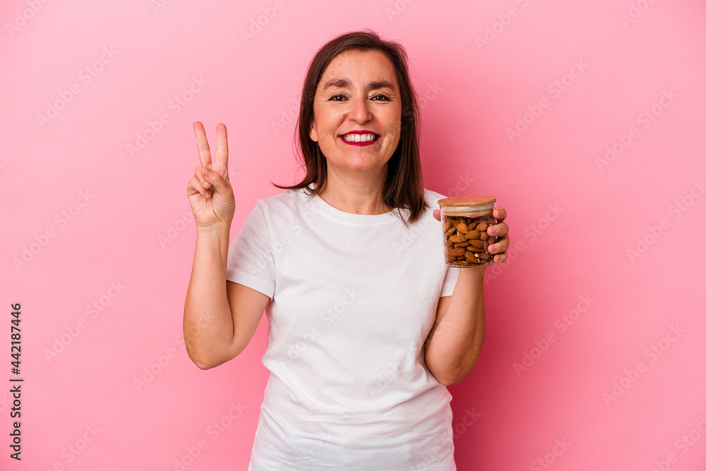 Middle age caucasian woman holding an almond jar isolated on pink background showing number two with fingers. Middle age caucasian woman holding an almond jar isolated on pink background showing number two with fingers.
