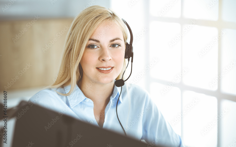 Blonde business woman sitting and communicated by headset in call center in sunny office. Concept of telesales business Blonde business woman sitting and communicated by headset in call center in sunny office. Concept of telesales business