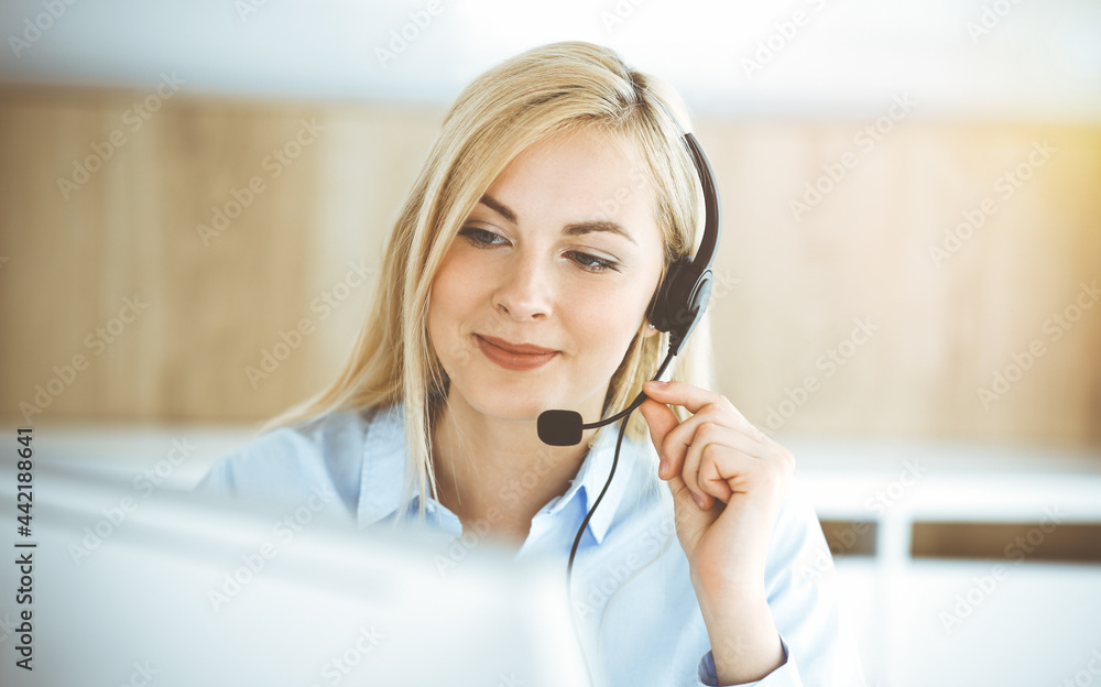 Blonde business woman sitting and communicated by headset in call center in sunny office. Concept of telesales business Blonde business woman sitting and communicated by headset in call center in sunny office. Concept of telesales business