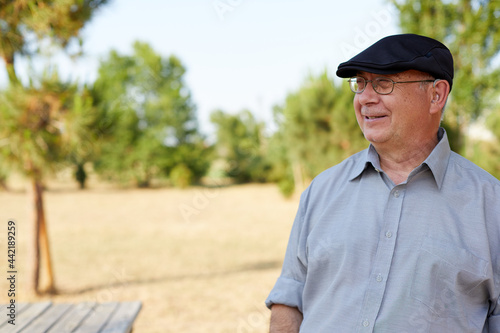 old man smiling with hearing aid hat and glasses outdoor