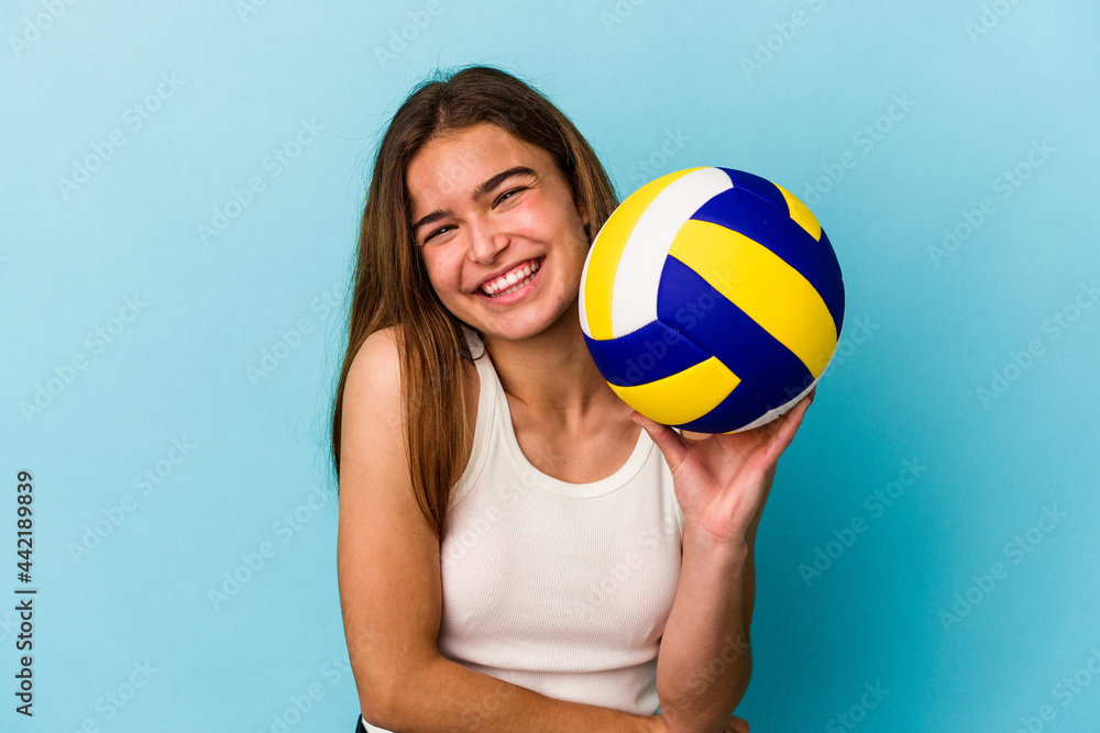Young caucasian woman playing volleyball isolated on blue background laughing and having fun.