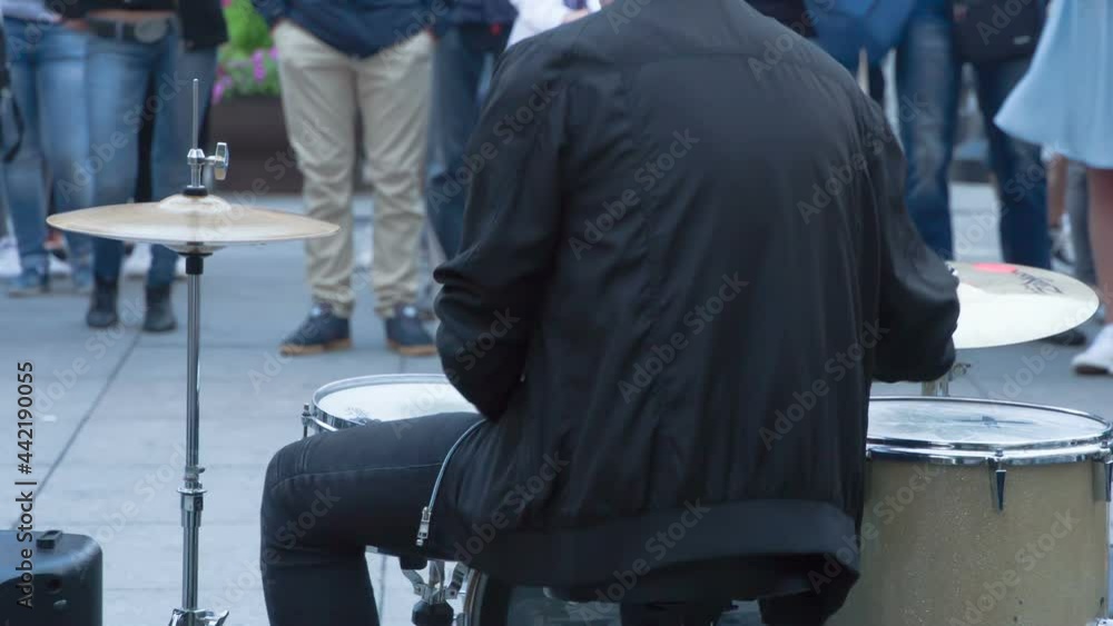 Drummer Plays for Passersby. A view of the musician's drummer from the back. He plays drums on the background of unrecognized listeners Drummer Plays for Passersby. A view of the musician's drummer from the back. He plays drums on the background of unrecognized listeners