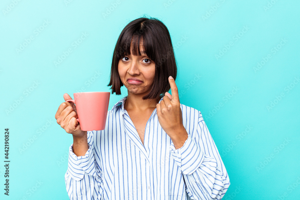 Young mixed race woman holding a pink mug isolated on blue background pointing with finger at you as if inviting come closer. Young mixed race woman holding a pink mug isolated on blue background pointing with finger at you as if inviting come closer.