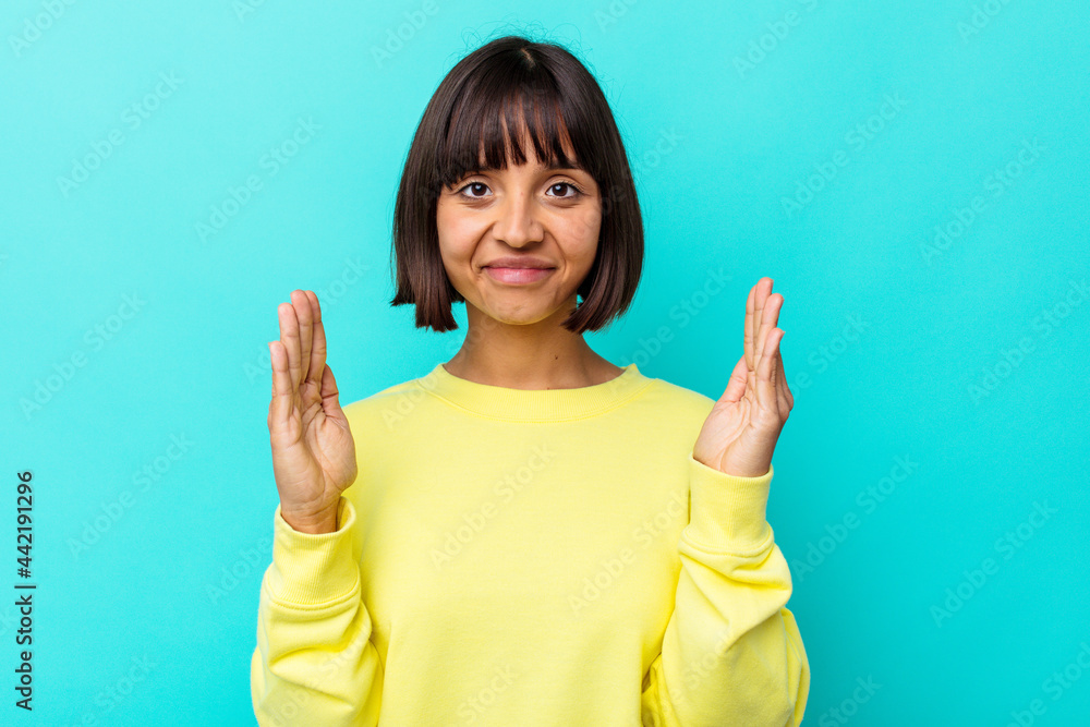 Young mixed race woman isolated on blue background holding something little with forefingers, smiling and confident. Young mixed race woman isolated on blue background holding something little with forefingers, smiling and confident.