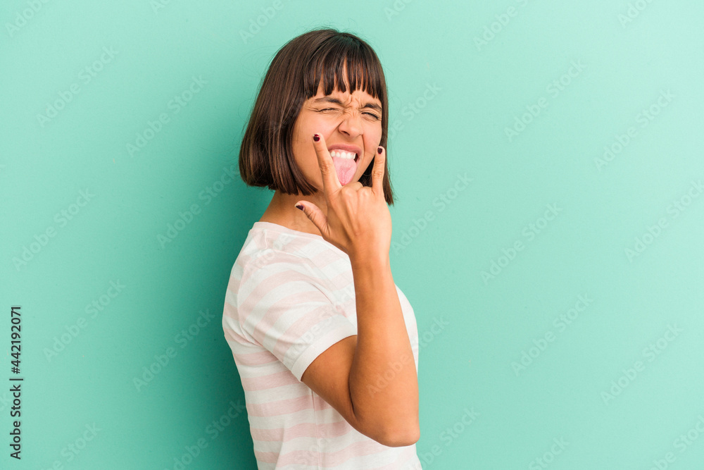 Young mixed race woman isolated on blue showing rock gesture with fingers Young mixed race woman isolated on blue showing rock gesture with fingers