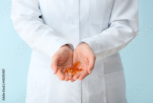 Female doctor holding fish oil pills on color background, closeup