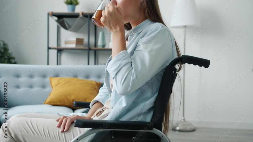 Slow motion portrait of young disabled lady drinking tea sitting in wheelchair alone in apartment. Physical disability and leisure time concept. Slow motion portrait of young disabled lady drinking tea sitting in wheelchair alone in apartment. Physical disability and leisure time concept.