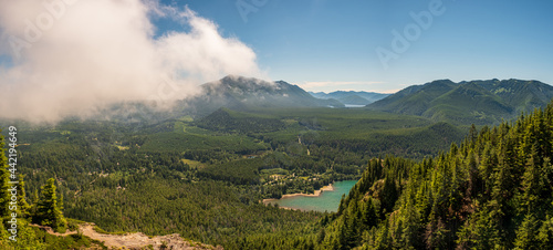 A fog cover hides a forested valley and blue lake below