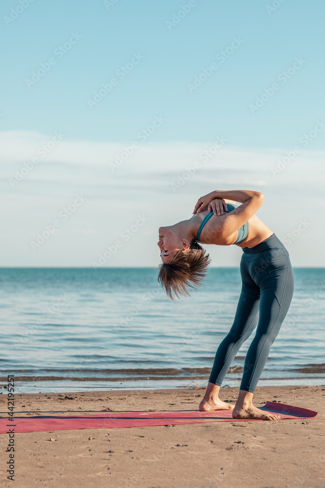 Naklejka premium a young attractive woman, of Asian appearance, practicing yoga, performs a stretching exercise, on the beach