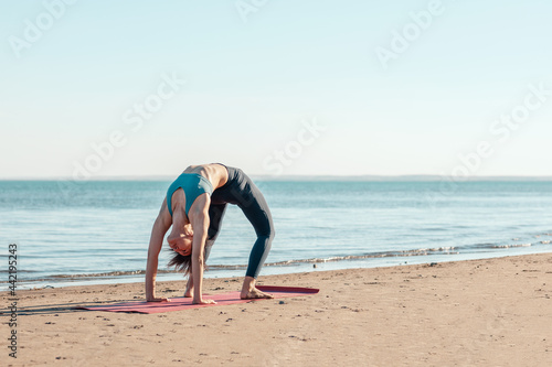 a young attractive woman, of Asian appearance, practicing yoga, performs a stretching exercise, on the beach. urdhva dhanurasana, bow pose face down.