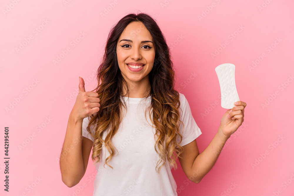Young mexican woman holding a compress isolated on pink background smiling and raising thumb up Young mexican woman holding a compress isolated on pink background smiling and raising thumb up