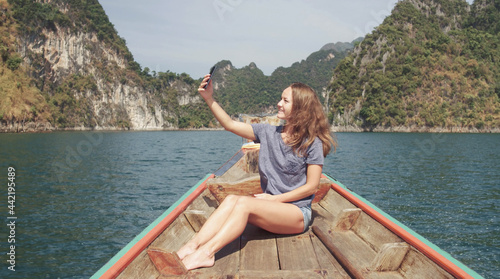 Young Happy Mixed Race Girl Sitting and Relaxing on Traditional Thai Wooden Long Tail Boat at Khao Sok Lake. Phang Nga Province, Thailand. © skymediapro