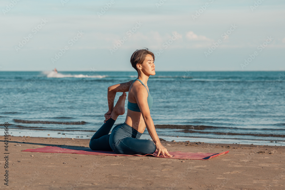 a young attractive woman, of Asian appearance, practicing yoga, performs a stretching exercise, on the beach. the Eka Pada Rajakapotasana, the pigeon pose