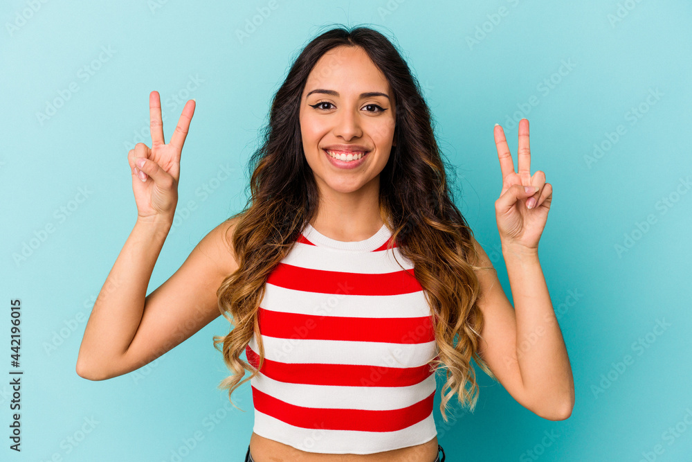 Young mexican woman isolated on blue background showing victory sign and smiling broadly. Young mexican woman isolated on blue background showing victory sign and smiling broadly.