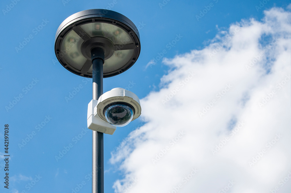 A CCTV camera is mounted on a pillar with a blue sky and clouds in the background. A CCTV camera is mounted on a pillar with a blue sky and clouds in the background.