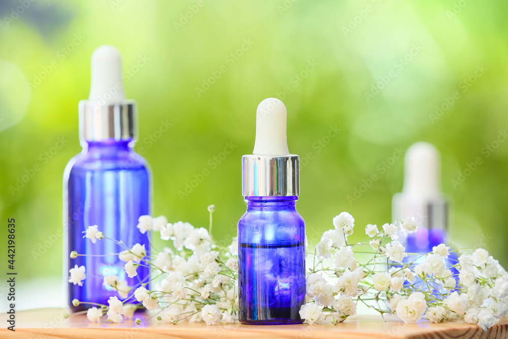 Bottles of essential oil and flowers on table outdoors, closeup Bottles of essential oil and flowers on table outdoors, closeup