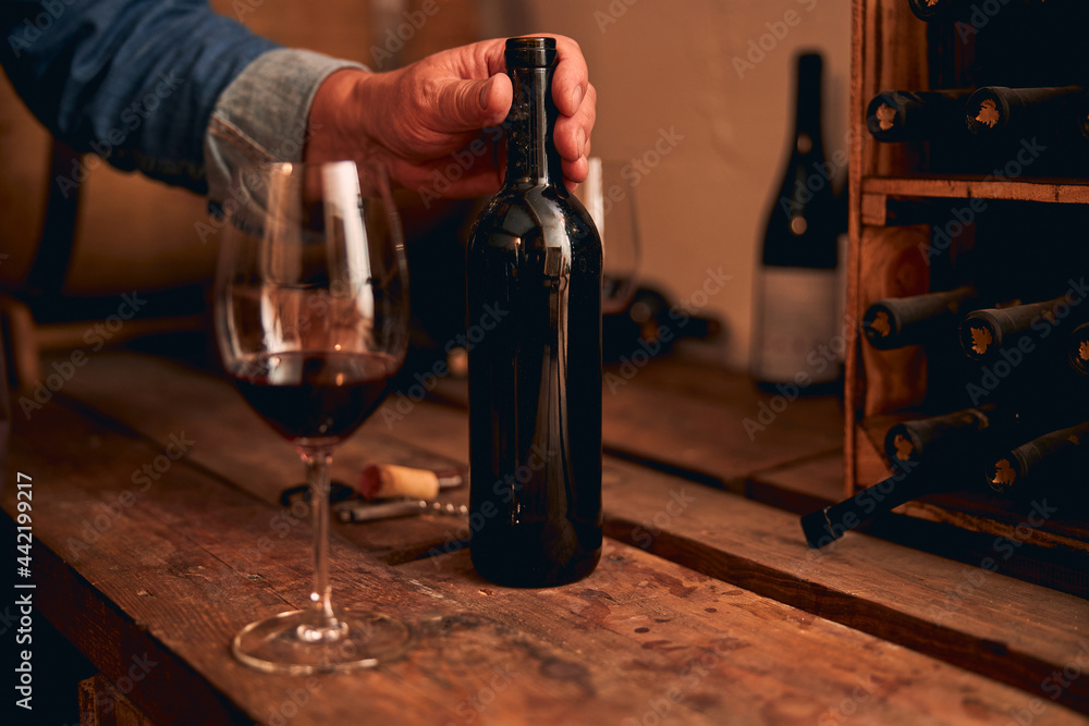Hand touching unlabeled bottle of red wine Hand touching unlabeled bottle of red wine
