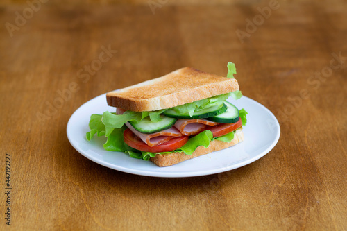 sandwich with ham and vegetables.tasty sandwich with ham, green salad, cucumbers and tomatoes on the wooden background.toasted homemade sandwich with fresh vegetables on the white plate.copy space