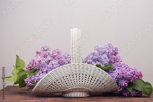 Fototapeta Naklejka Na Ścianę i Meble -  Beautiful white vintage wicker basket on a wooden table. Lilac flowers in a retro basket