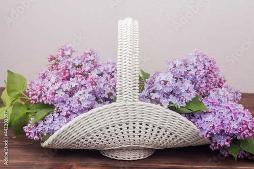 Fototapeta Naklejka Na Ścianę i Meble -  Beautiful white vintage wicker basket on a wooden table. Lilac flowers in a retro basket