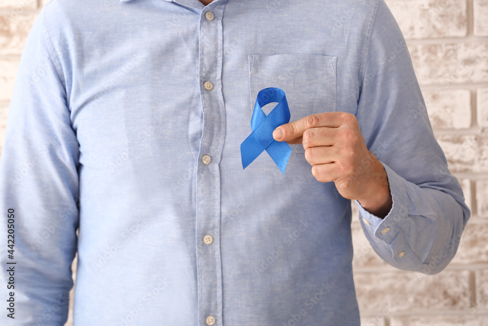 Fototapeta premium Man with blue ribbon near light brick wall, closeup. Colon cancer concept