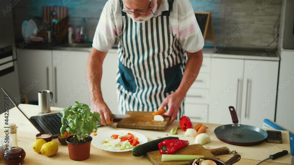 Grandfather participates in a group online competition in cooking from home. Old man counts down his hand and starts making a vegan somersault for an online competition using a laptop Grandfather participates in a group online competition in cooking from home. Old man counts down his hand and starts making a vegan somersault for an online competition using a laptop