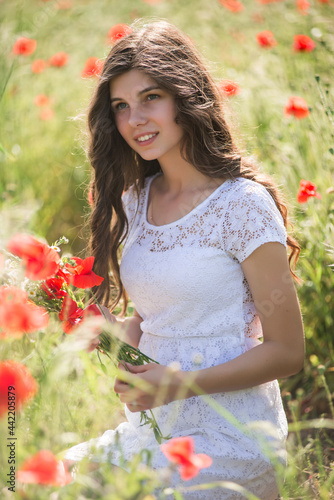 Beautiful girl in white dress on poppy field at summertime daylight