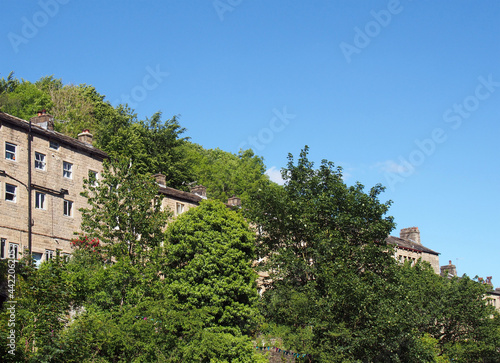 a row of traditional tall houses on a hillside surrounded by trees in summer in hebden bridge west yorkshire