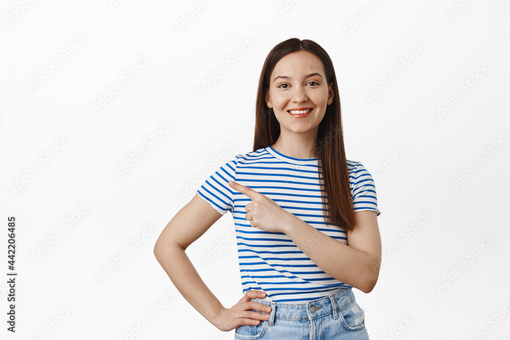 Portrait of young brunette woman pointing finger left, showing sale promo, point at logo, smiling happy, recommend click on link, standing over white background Portrait of young brunette woman pointing finger left, showing sale promo, point at logo, smiling happy, recommend click on link, standing over white background