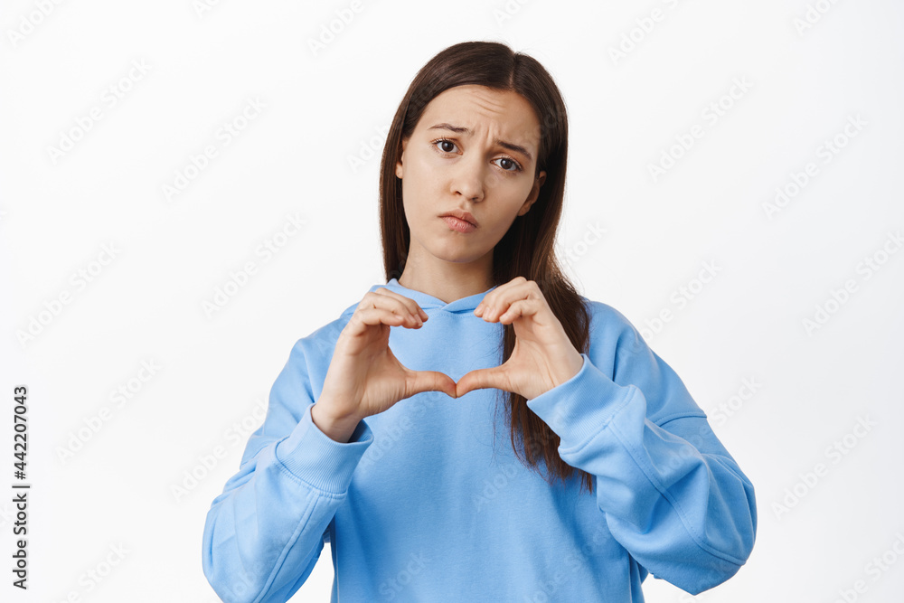 Heartbroken girl showing broken heart and looking gloomy, upset about breakup with love partner, standing moody against white background Heartbroken girl showing broken heart and looking gloomy, upset about breakup with love partner, standing moody against white background