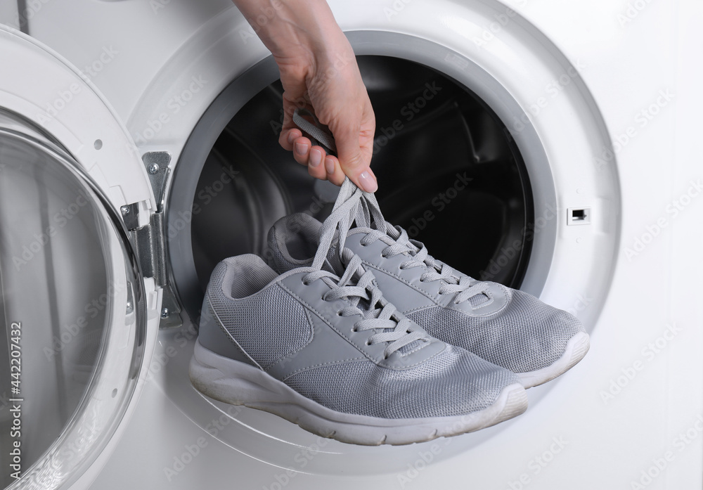 Woman putting pair of sport shoes into washing machine, closeup Woman putting pair of sport shoes into washing machine, closeup