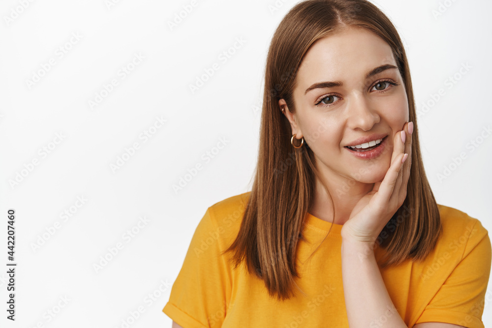 Beauty and women. Close up of attractive blond girl touch clean, no make up glowing skin, hold hand on cheek, concept of skin care and facial cosmetics, white background Beauty and women. Close up of attractive blond girl touch clean, no make up glowing skin, hold hand on cheek, concept of skin care and facial cosmetics, white background
