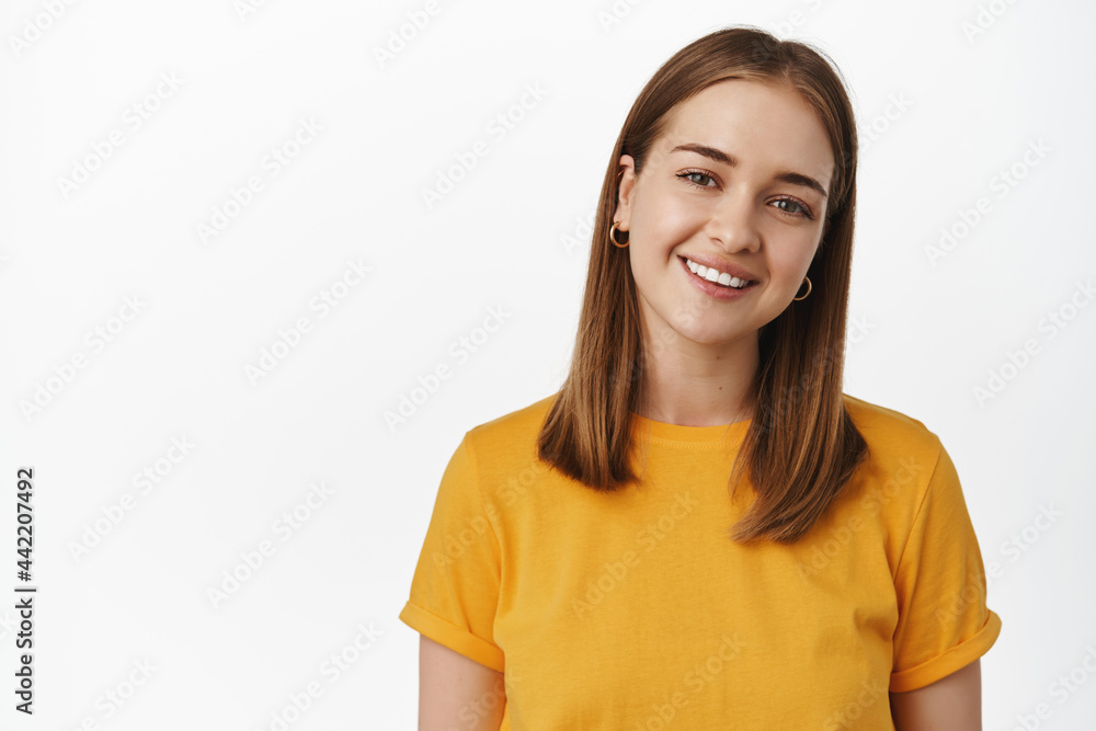 Portrait of candid young woman smiling white teeth, tilt head friendly and looking happy at camera, wearing yellow t-shirt against white background Portrait of candid young woman smiling white teeth, tilt head friendly and looking happy at camera, wearing yellow t-shirt against white background