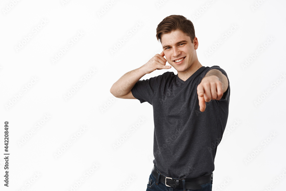 Call me. Smiling charismatic guy, modern young man show phone calling gesture and pointing finger at camera, inviting you, luring to contact him, white background Call me. Smiling charismatic guy, modern young man show phone calling gesture and pointing finger at camera, inviting you, luring to contact him, white background