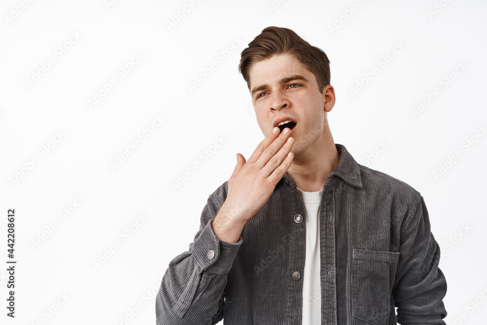 Image of handsome stylish guy, student yawning and cover opened mouth, yawn from boredom, feeling uninterested, careless and unamused, white background Image of handsome stylish guy, student yawning and cover opened mouth, yawn from boredom, feeling uninterested, careless and unamused, white background