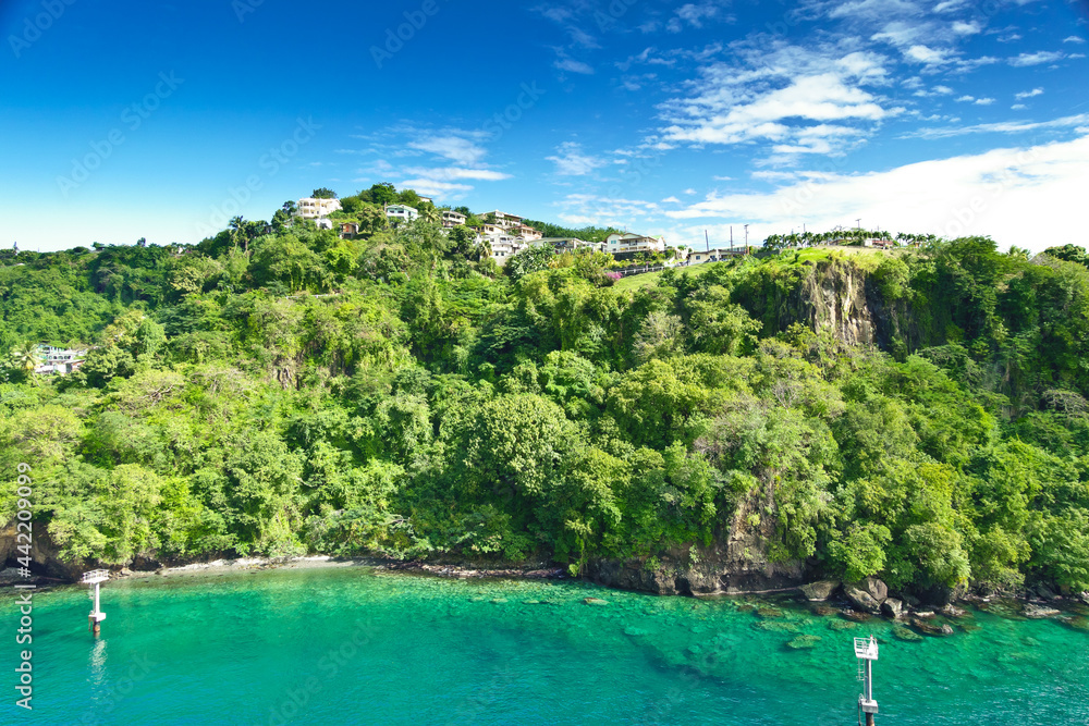 Coastline at Kingstown on Saint Vincent, steep cliff covered by trees behind turquoise and emerald colored water