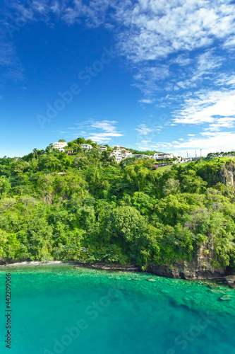 Coastline at Kingstown on Saint Vincent, steep cliff covered by trees behind turquoise and emerald colored water