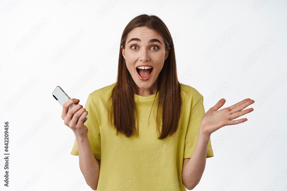 Portrait of excited brunette girl hold smartphone, great big news on mobile phone, thrilled with awesome notification, online discounts, white background Portrait of excited brunette girl hold smartphone, great big news on mobile phone, thrilled with awesome notification, online discounts, white background
