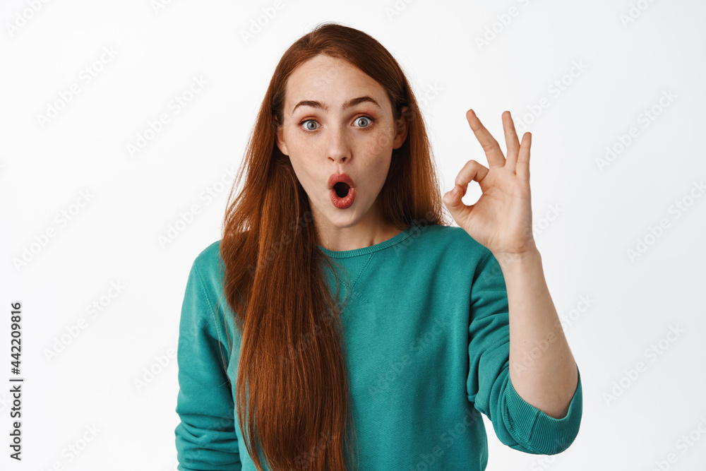 Surprised and impressed ginger girl look in awe, gasp and say wow, show okay zero gesture, OK sign, praise and compliment great thing, white background Surprised and impressed ginger girl look in awe, gasp and say wow, show okay zero gesture, OK sign, praise and compliment great thing, white background