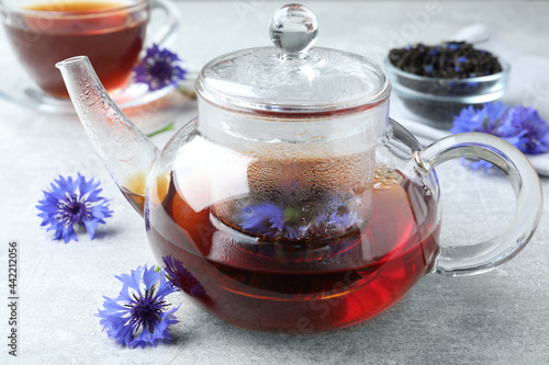 Glass pot with tea and cornflowers on light table, closeup