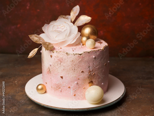 A trendy home-made pink cake decorated with a large flower and golden balls. Modern wafer paper cake decorations