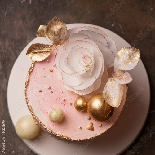 A trendy home-made pink cake decorated with a large flower and golden balls, top view.  Wafer paper cake.