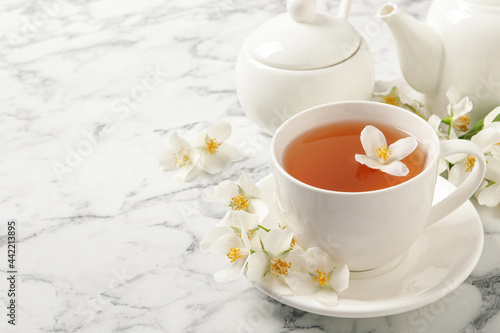 Aromatic jasmine tea and fresh flowers on white marble table, space for text