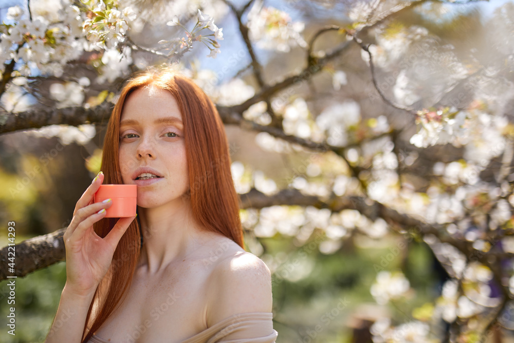 good-looking caucasian female using moisturizing cream posing in spring garden with blooming trees with white leaves flowers. copy space for advertisement. natural beauty concept good-looking caucasian female using moisturizing cream posing in spring garden with blooming trees with white leaves flowers. copy space for advertisement. natural beauty concept
