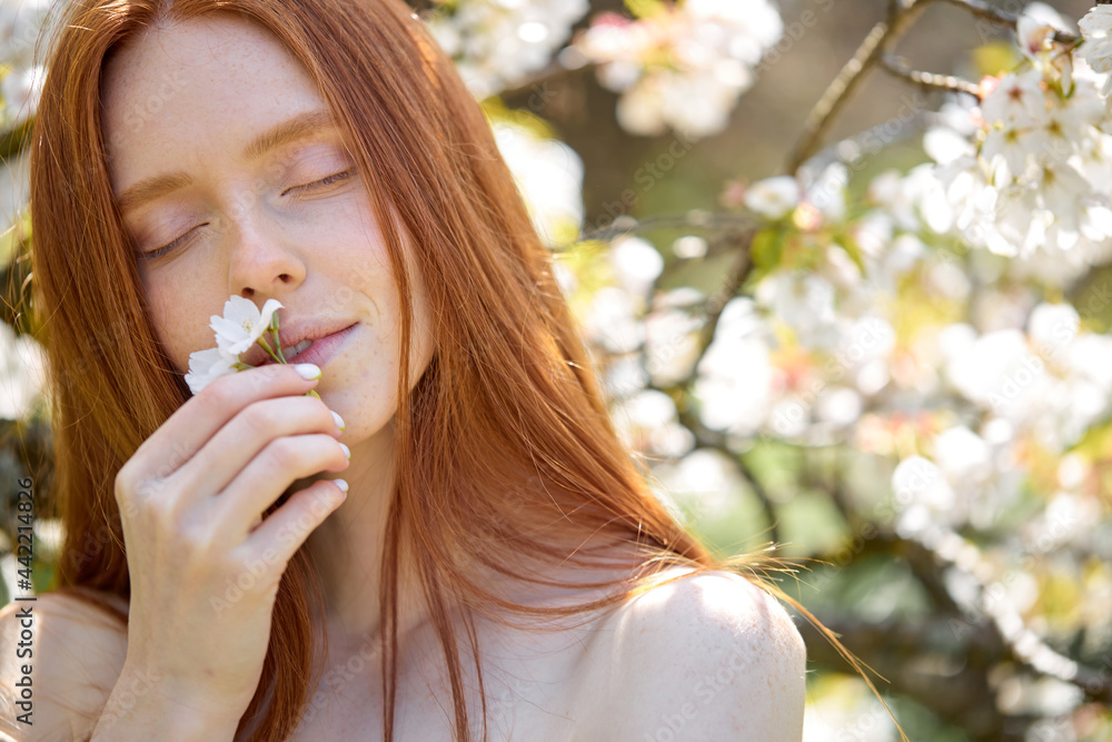 close-up portrait of beautiful redhead woman in spring garden. female inhales the fragrance of flowering trees with eyes closed, natural make-up. copy space close-up portrait of beautiful redhead woman in spring garden. female inhales the fragrance of flowering trees with eyes closed, natural make-up. copy space